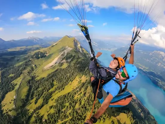 High altitude summer tandem paragliding flight above green Swiss Alps and lakes