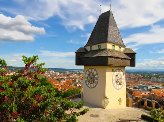 The iconic Uhrturm clock tower on top of Schlossberg hill under a blue sky.