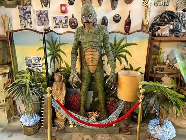 A life-sized Creature from the Black Lagoon statue displayed in a tropical tiki-themed room with masks.