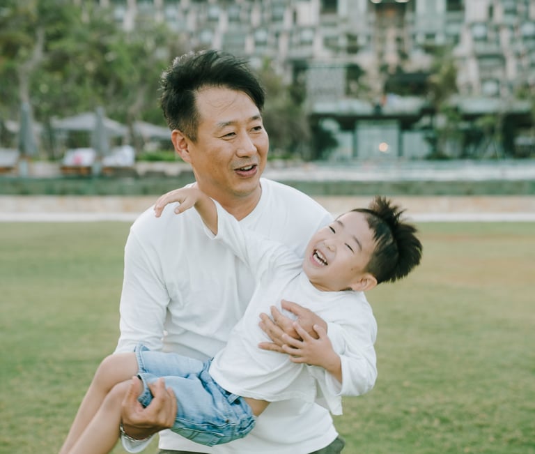 Father and son playful moment during a family photography session at The Apurva Kempinski Bali lawn area.