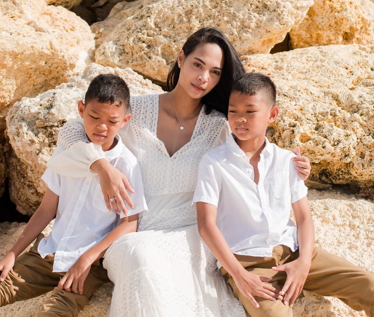 Ayunda mother with her two sons sitting by the rocks at Melasti Beach during a natural family photography session in Bali.