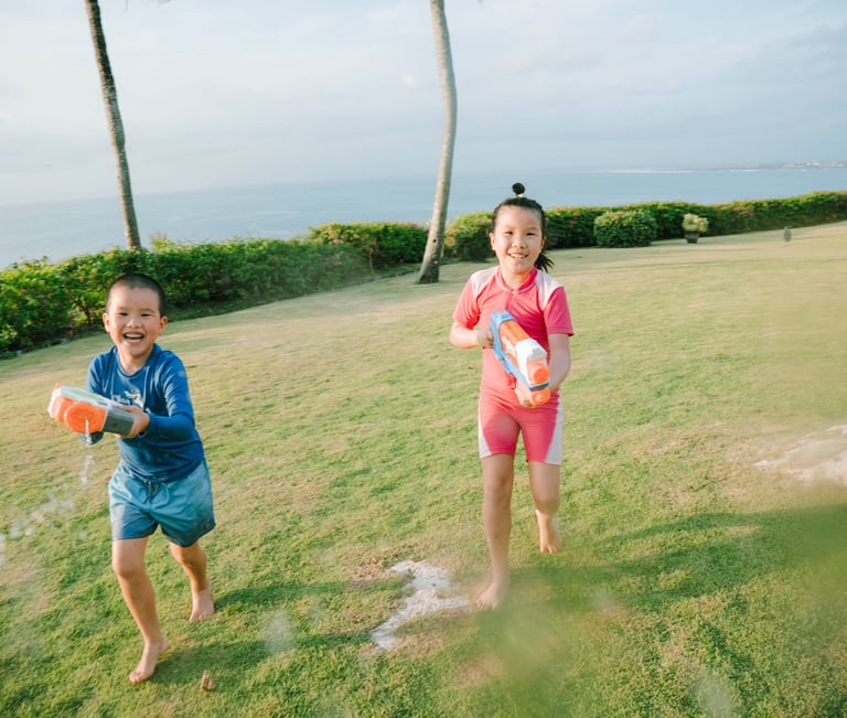 two Children playing with water guns during a family photography session at AYANA Villas Jimbaran Bali