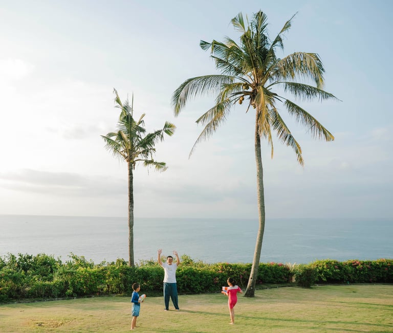 Father and children playing water gun on the oceanfront lawn at AYANA Villas Jimbaran Bali