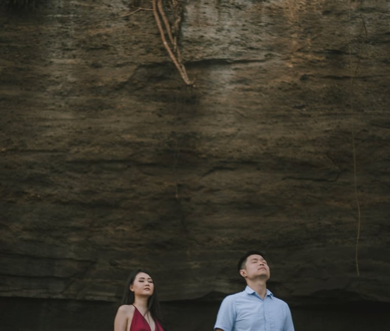 Romantic couple standing under cliff wall at Pantai Nyanyi Bali during sunset.