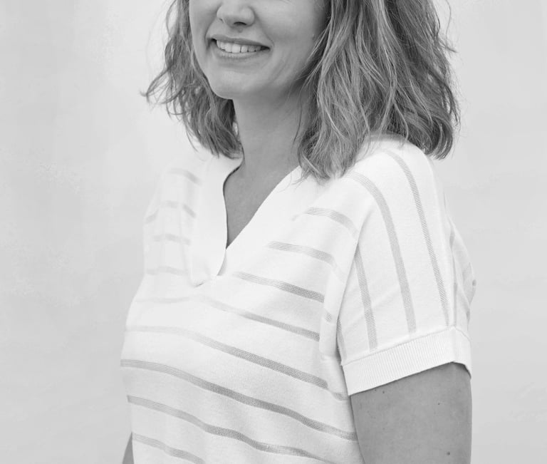 A black and white professional portrait of a smiling woman with wavy hair wearing a striped shirt.