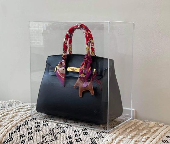 Designer bag in an acrylic display case on a sofa.