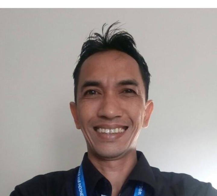 Smiling man in a black button-down shirt with a blue lanyard posing for a professional headshot.