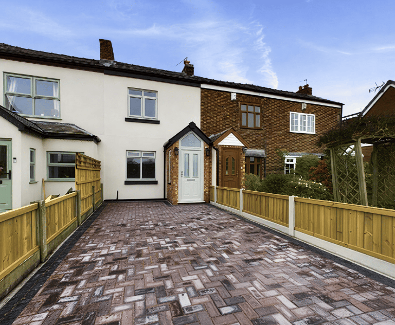 A modern block paved driveway and wooden panel fencing in front of a white semi-detached house.