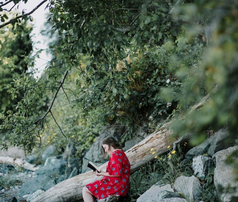 a woman in a red dress sitting on a log reading the bible