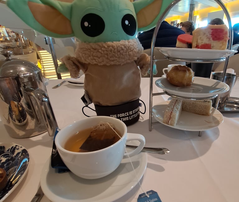 Little Green stuffed Animal on table with Tea cup and cakes