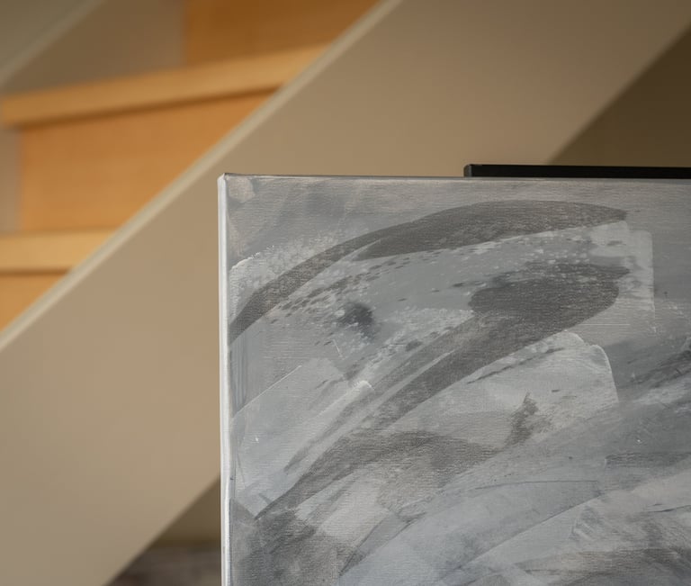 Close-up of a grey abstract canvas painting on an easel in a modern home with wooden stairs.