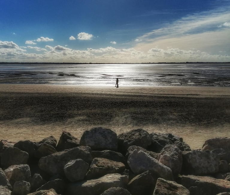 une personne debout sur une plage avec des rochers et la mer au coucher de soleil 