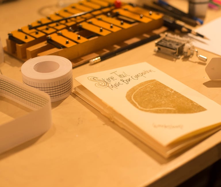 a table with a glockenspiel and a zine about music box composition