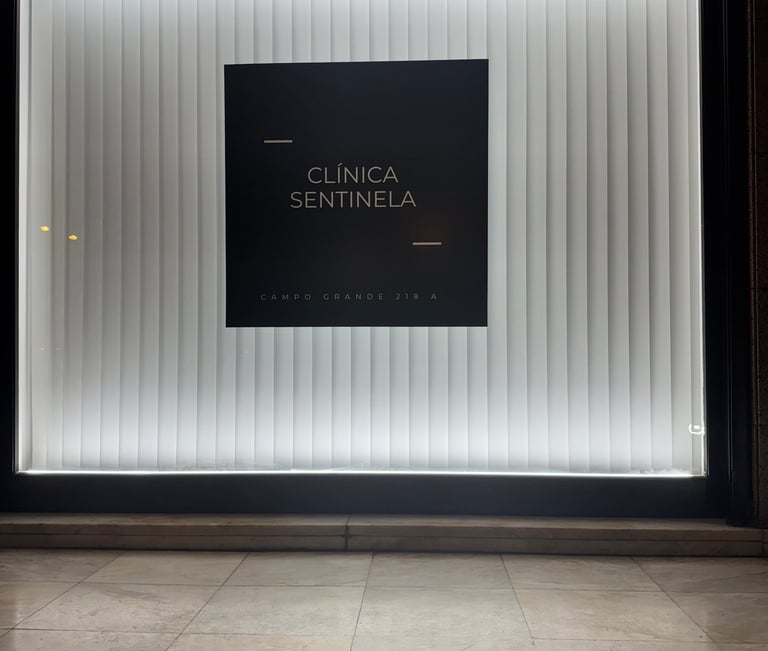 Illuminated Clínica Sentinela storefront window with black logo signage and white vertical blinds.