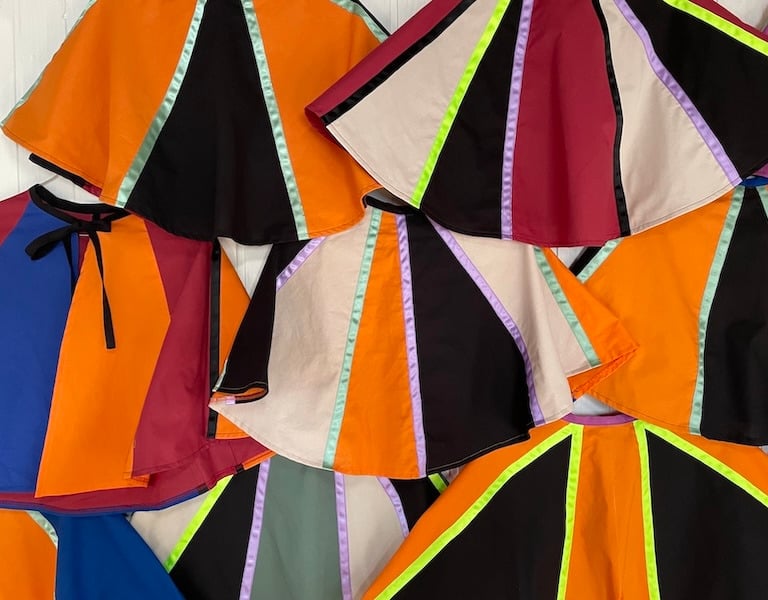 Handmade colorful circle capes with vibrant ribbon stripes in orange, black, and maroon fabric.