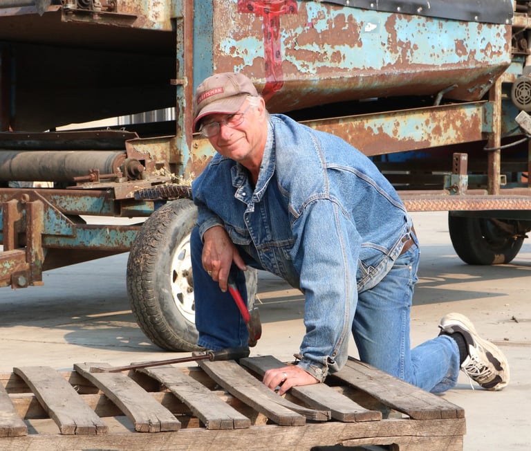 Bob Proctor in work denim, kneeling by a pallet on the ground outside at Poplar Bluff Organics