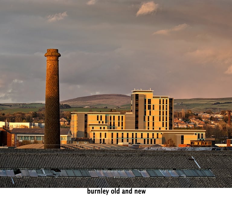 an old brick building with a chimney with new architecture of burnley centre in the background