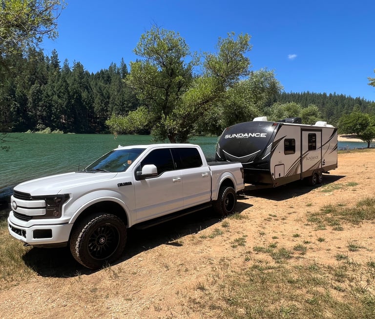 white ford f150 hooked to camping trailer in front of rollins lake