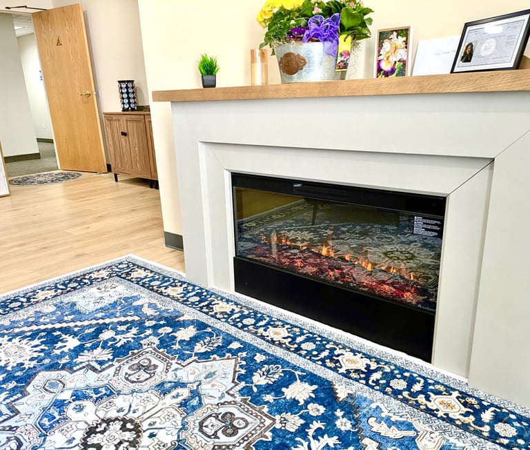Modern electric fireplace with white mantel and blue patterned area rug in a cozy office waiting room.