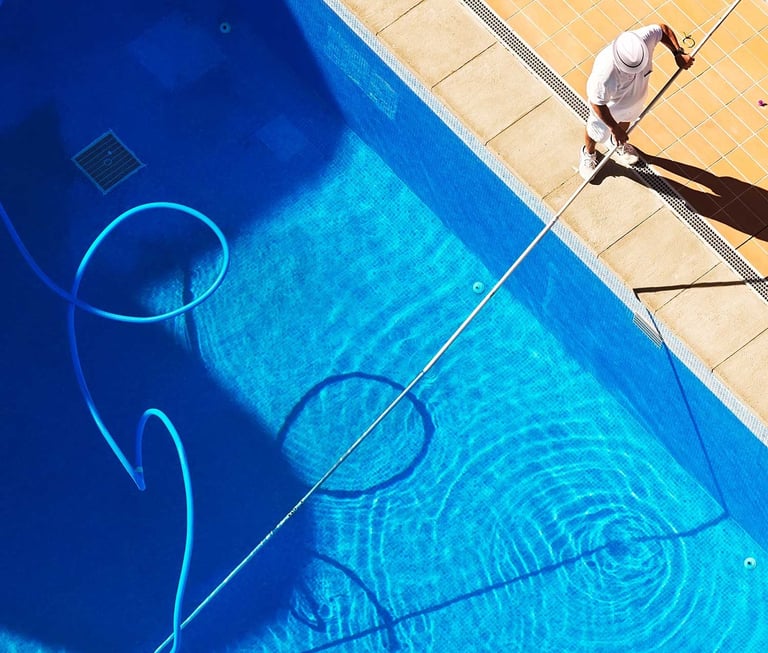 Technician using a vacuum pole to clean a backyard pool—illustrating weekly pool maintenance service in action.