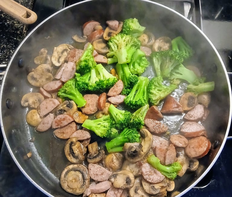 Sautéing mushrooms and sausage in a pan for alfredo pasta