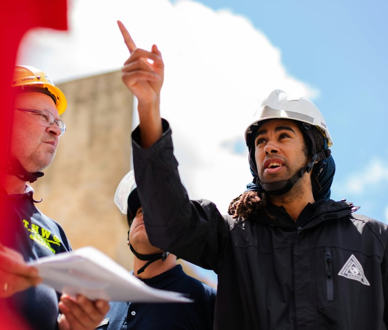Professional construction site supervisor in a hard hat pointing toward project plans during a team meeting.
