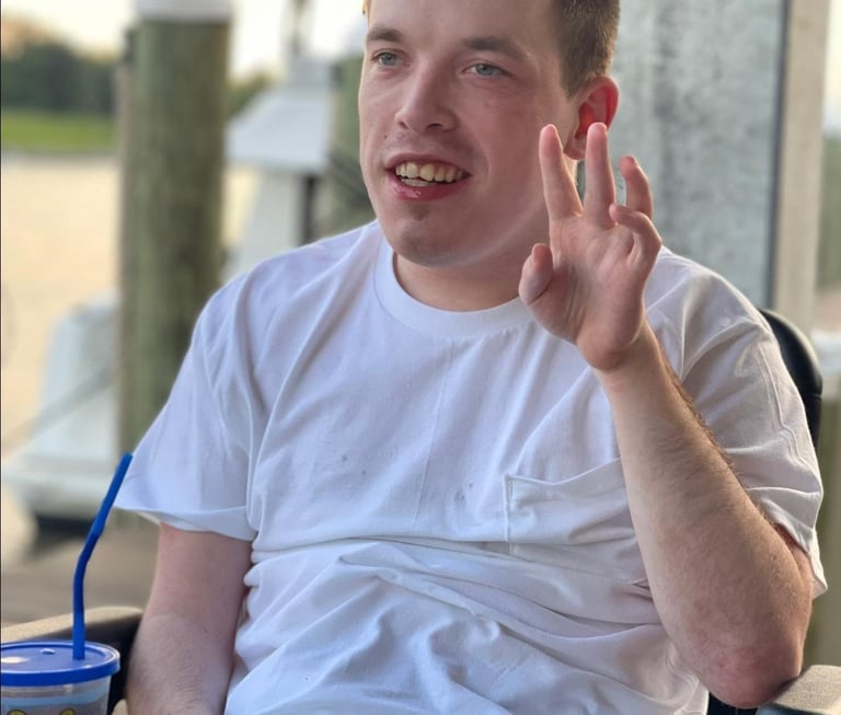 Smiling young man in a wheelchair enjoying a sunny day at an outdoor waterfront restaurant.