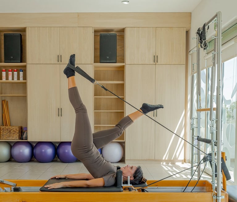 Woman lying on a Pilates Reformer doing a leg exercise using the foot straps in the Cabo San Lucas studio.