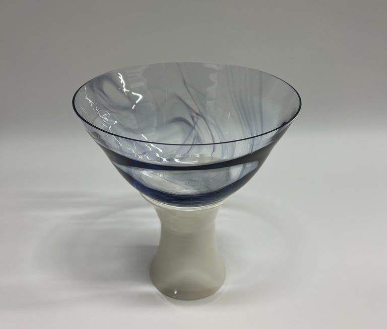 Large and wide blown glass bowl, with swirls of ink blue glass, on a white porcelain ceramic base. 