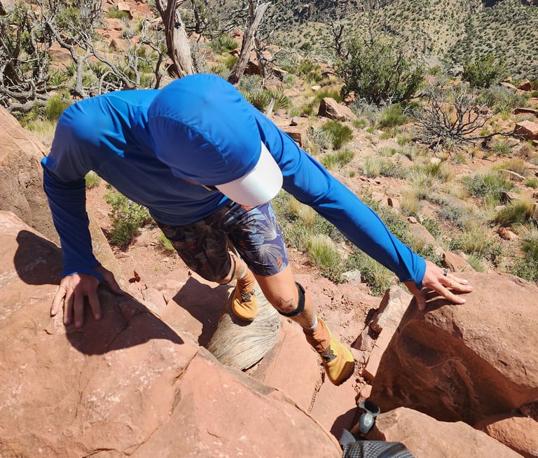 Moose descending a steep red sandstone cliff in the Grand Canyon wearing orange Topo Mountain Racers