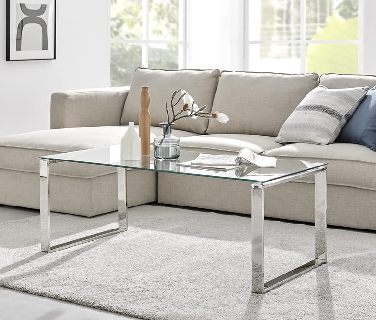 Modern rectangular glass coffee table with chrome legs in a bright living room setup.