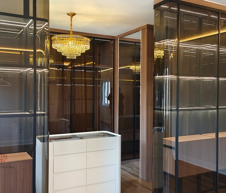 Modern luxury walk-in closet with gold crystal chandelier, LED-lit glass shelving, and white island dresser.