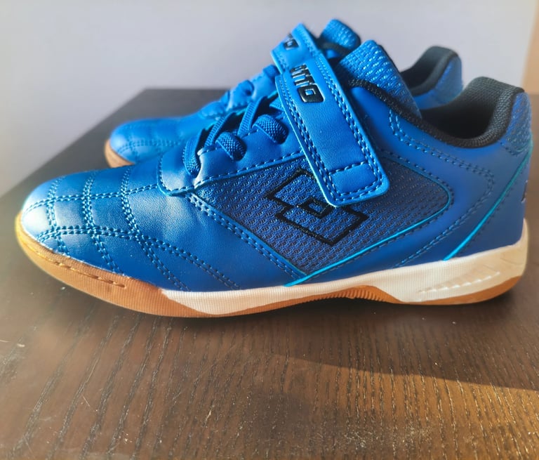 Sapatilha infantil Lotto azul com velcro e sola laranja vista de lado numa mesa de madeira