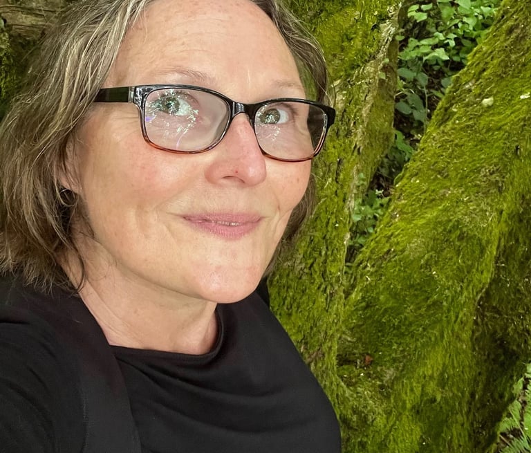 a woman in glasses and a black shirt is taking a selfie in nature