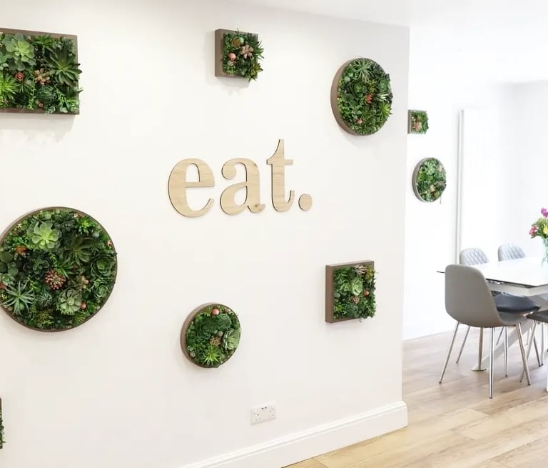 Modern dining room featuring framed succulent wall art and an 'eat' sign next to a white table.