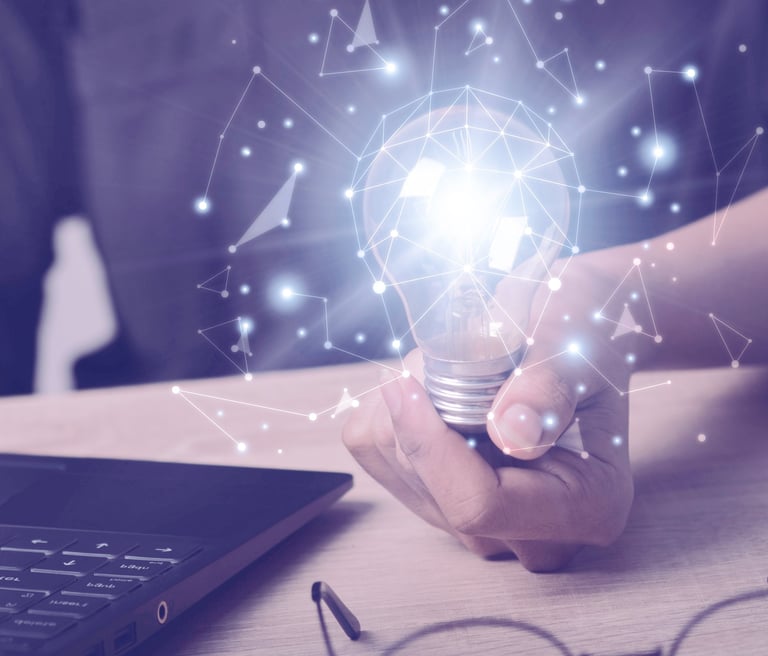 A person's hand holding a light bulb next to a laptop.