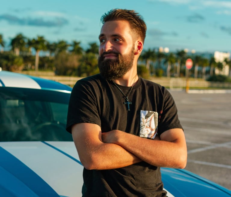 white man with a beard looking to the side sitting on a blue car hood