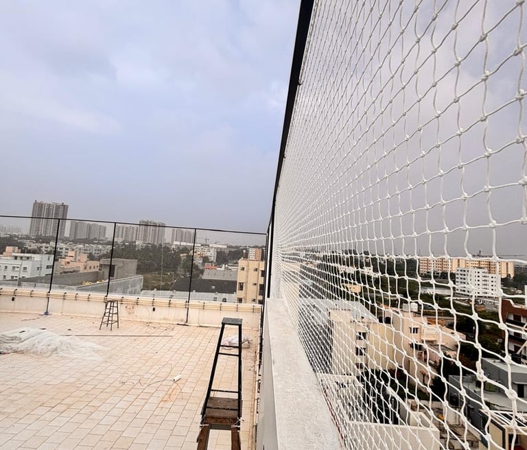 A technician carefully installing a sturdy sports net on a rooftop terrace under a clear blue sky in