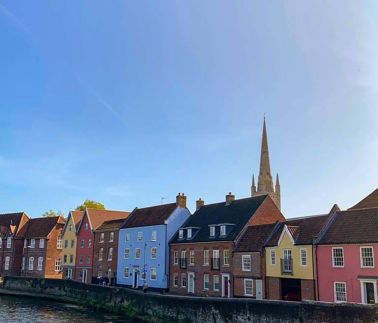 a beautiful still of colourful houses on the Norwich river with the cathedral in the background