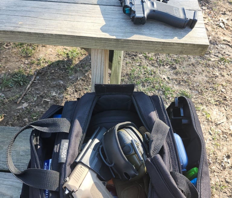 Black bag with ear protection and 2 self-defense firearms one with red dot one without.