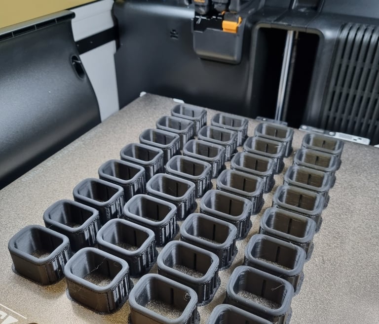 A Bambu Lab 3D printer batch producing black filament components on a textured build plate.