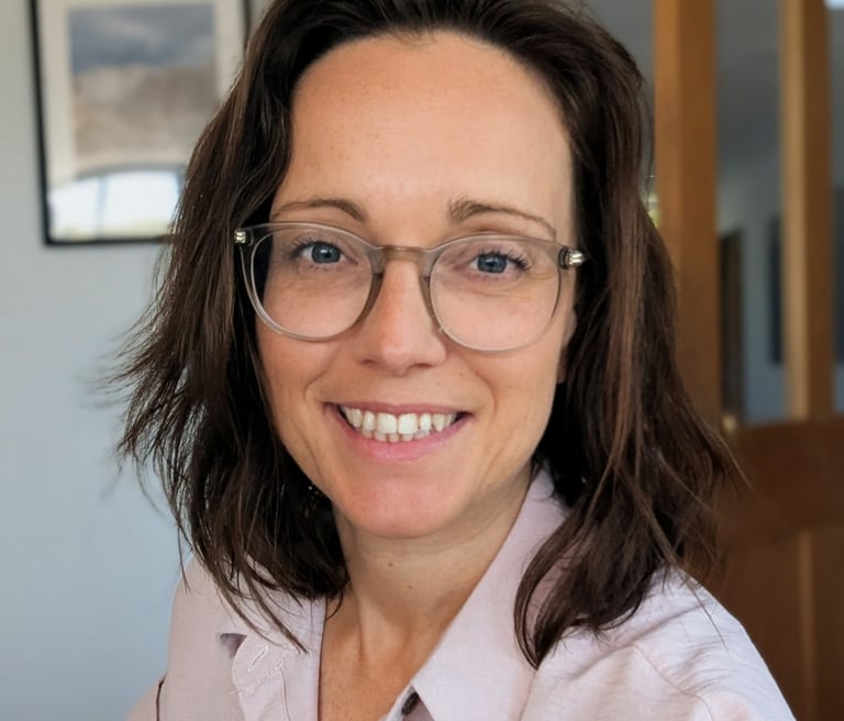 A smiling female kent tutor with brown hair wearing transparent glasses and a pink shirt.