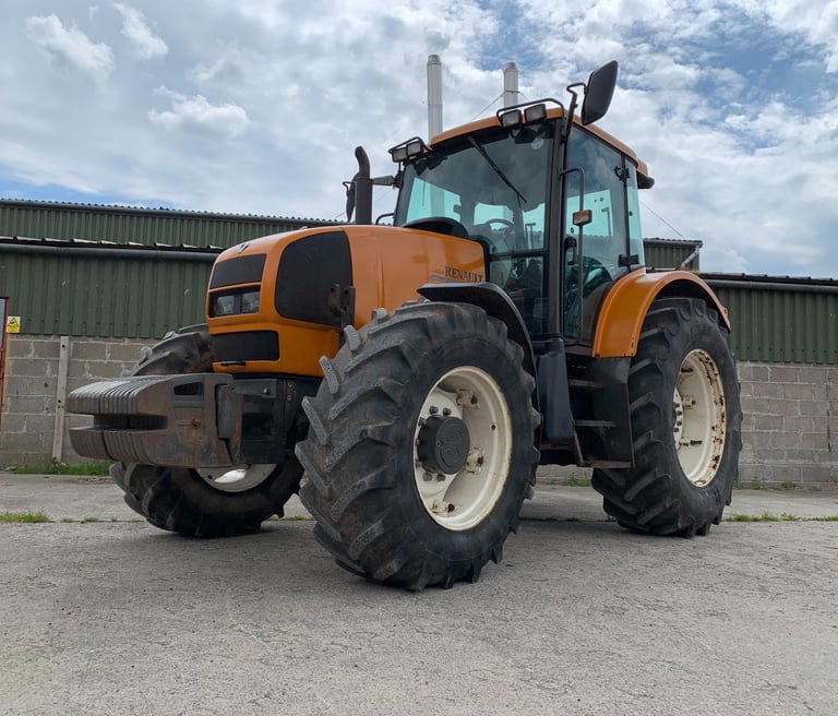 A large orange Renault agricultural tractor parked on a concrete yard in front of a farm building.