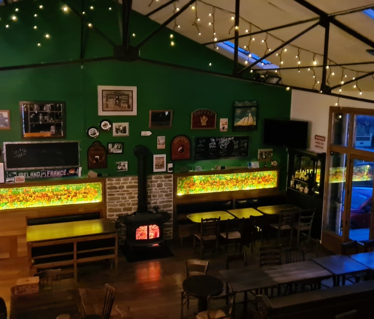 Cozy Irish pub interior with green walls, wood stove, fairy lights, and seating area.