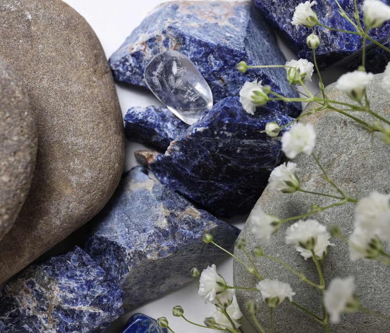 Cristales naturales de sodalita azul y piedras de río pulidas combinadas con flores blancas.