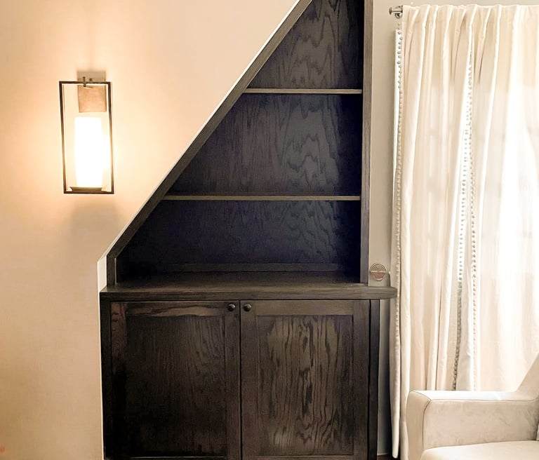 Asymmetrical wooden bookcase and cabinet built in to fit an odd-sized space in a client home.