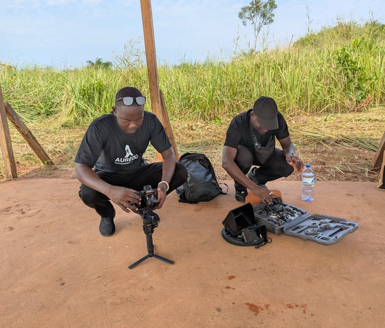 Two videographers set up professional camera equipment and a gimbal stabilizer for an outdoor field shoot.