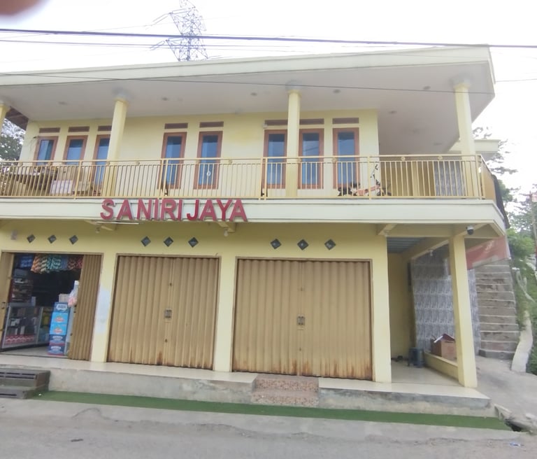 Saniri Jaya storefront in Indonesia with yellow two-story building and metal rolling doors.