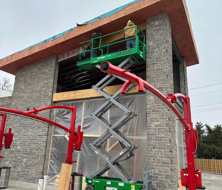 Construction workers using a green scissor lift to install a roof on a new stone commercial building.