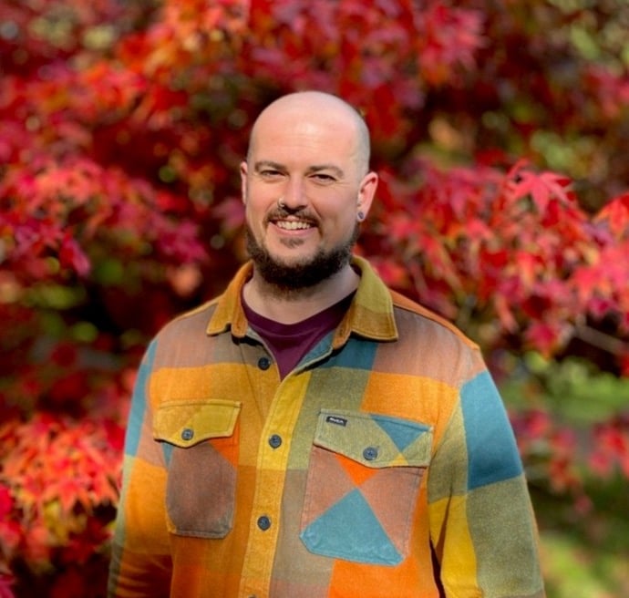 Sam rayes creative bio pic smiling with autumnal trees as a background